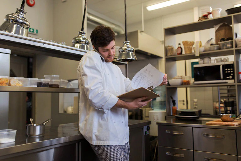 تصویر آشپز یک رستوران با برگه‌های موجودی در دست